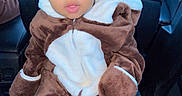 Maziyon is registered to the contest to win money with this photo: baby, child, car_interior, seat, seatbelt, fuzzy_outfit, brown_clothing, white_clothing, face, eyes, headrest, hand, tissue, curious_expression, sitting, portrait, indoors, person, cute, cozy