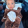 baby, child, car_interior, seat, seatbelt, fuzzy_outfit, brown_clothing, white_clothing, face, eyes, headrest, hand, tissue, curious_expression, sitting, portrait, indoors, person, cute, cozy