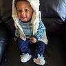 baby, child, smile, blue_clothing, striped_shirt, fluffy_vest, hood, slippers, dinosaur_slippers, black_chair, leather_chair, sitting, happy, cute, indoors, portrait, young_child, person, cozy, warm_clothing