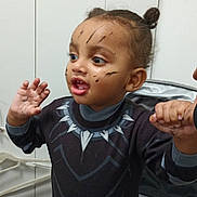 Noah joined the competition — help win amazing prizes! black_panther, child, clothing, costume, curious, expression, face, face_paint, furniture, gesture, hair_bun, hand_holding, indoor, person, portrait, smiling, stroller, toddler, toy, young_child