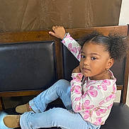 Noelie joined the competition — help win amazing prizes! child, girl, curly_hair, pigtails, sitting, bench, black_cushion, pink_butterfly_shirt, light_blue_jeans, brown_shoes, bracelet, earrings, necklace, indoor, wooden_bench, casual_clothing, portrait, looking_at_camera, young, relaxed