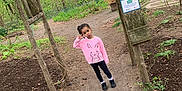 Melanie is registered to the contest to win money with this photo: child, girl, pink_sweater, bunny_design, peace_sign, outdoor, nature, trees, pathway, wooden_structure, sign, greenery, plants, forest, casual_clothing, playful, young, daylight, standing, posing