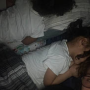 Melanie joined the competition — help win amazing prizes! child, children, sleeping, resting, bed, pillow, blanket, white_shirt, curly_hair, indoor, dim_light, adult, glasses, face_partial, close_together, dark, grainy, casual, family, home