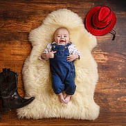 Lenny participe au concours pour gagner de l'argent avec cette photo : baby, infant, denim_overalls, smiling, face, fluffy_rug, wooden_floor, cowboy_boots, cowboy_hat, footwear, hat, child, portrait, happy, indoor, clothing, person, cute, lying_down, studio_photo