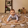 Lenny participe au concours pour gagner de l'argent avec cette photo : baby, child, indoor, rug, patterned_rug, tassels, wooden_floor, decorative_ladder, potted_plants, wooden_crate, chocolate_chicken, flower_pots, smiling, curious, crawling, long_sleeve_shirt, pants, floor, homedecor, portrait