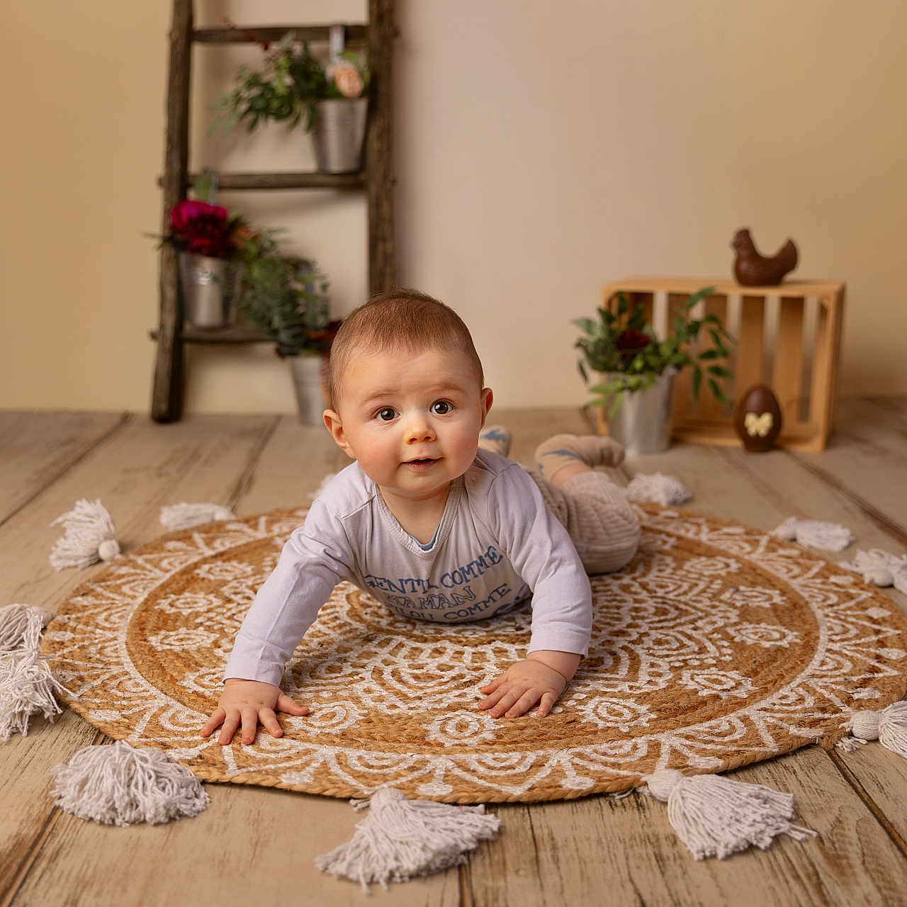 Lenny participe au concours pour gagner de l'argent avec cette photo : baby, child, indoor, rug, patterned_rug, tassels, wooden_floor, decorative_ladder, potted_plants, wooden_crate, chocolate_chicken, flower_pots, smiling, curious, crawling, long_sleeve_shirt, pants, floor, homedecor, portrait
