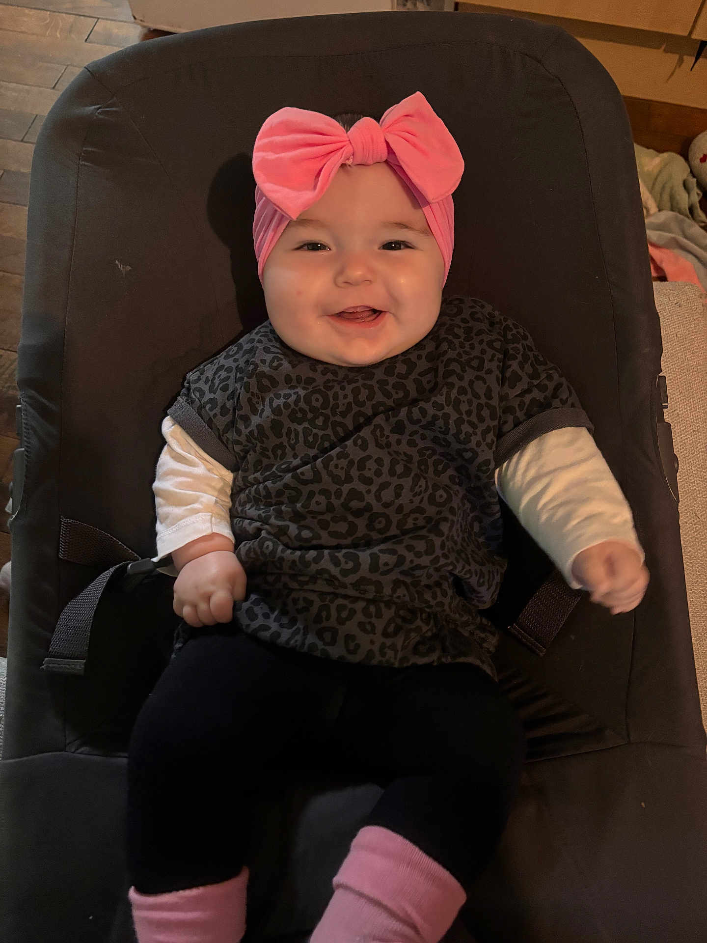 Noëlya participe au concours pour gagner de l'argent avec cette photo : baby, child, smiling, indoor, headband, pink, leopard_print, shirt, cushion, seat, legs, clothing, happy, portrait, infant, comfortable, wooden_floor, baby_seat, cute, person
