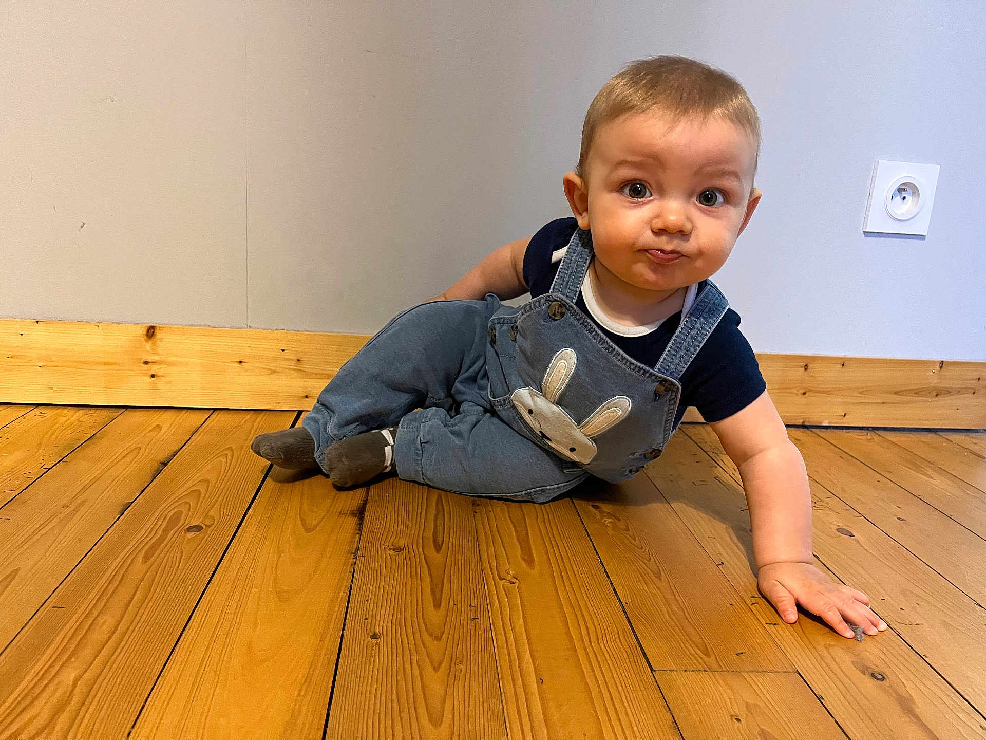 Marceau a rejoint le concours — aidez-le/la à gagner de superbes lots ! baby, infant, child, overalls, bunny_design, blue_clothing, wooden_floor, flooring, wall, power_socket, indoor, curious_expression, wide_eyes, cute, playful, person, one_child, crawling, casual, home