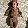 baby, infant, onesie, brown_clothing, hood, bear_ears, smile, lying_down, rug, soft_texture, indoors, person, feet, toes, happy, cute, child, cozy, portrait, home