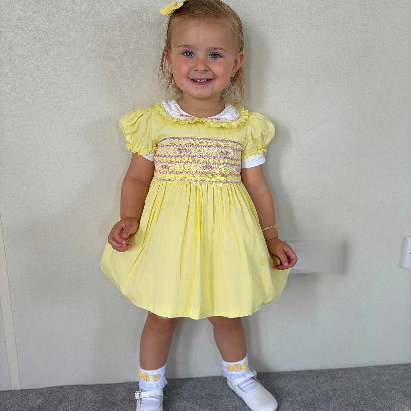 Christiana joined the competition — help win amazing prizes! bow, bracelet, carpet, child, cute, face, fashion, girl, happy, indoor, light_background, person, portrait, short_hair, smile, socks, standing, white_shoes, yellow_dress, young