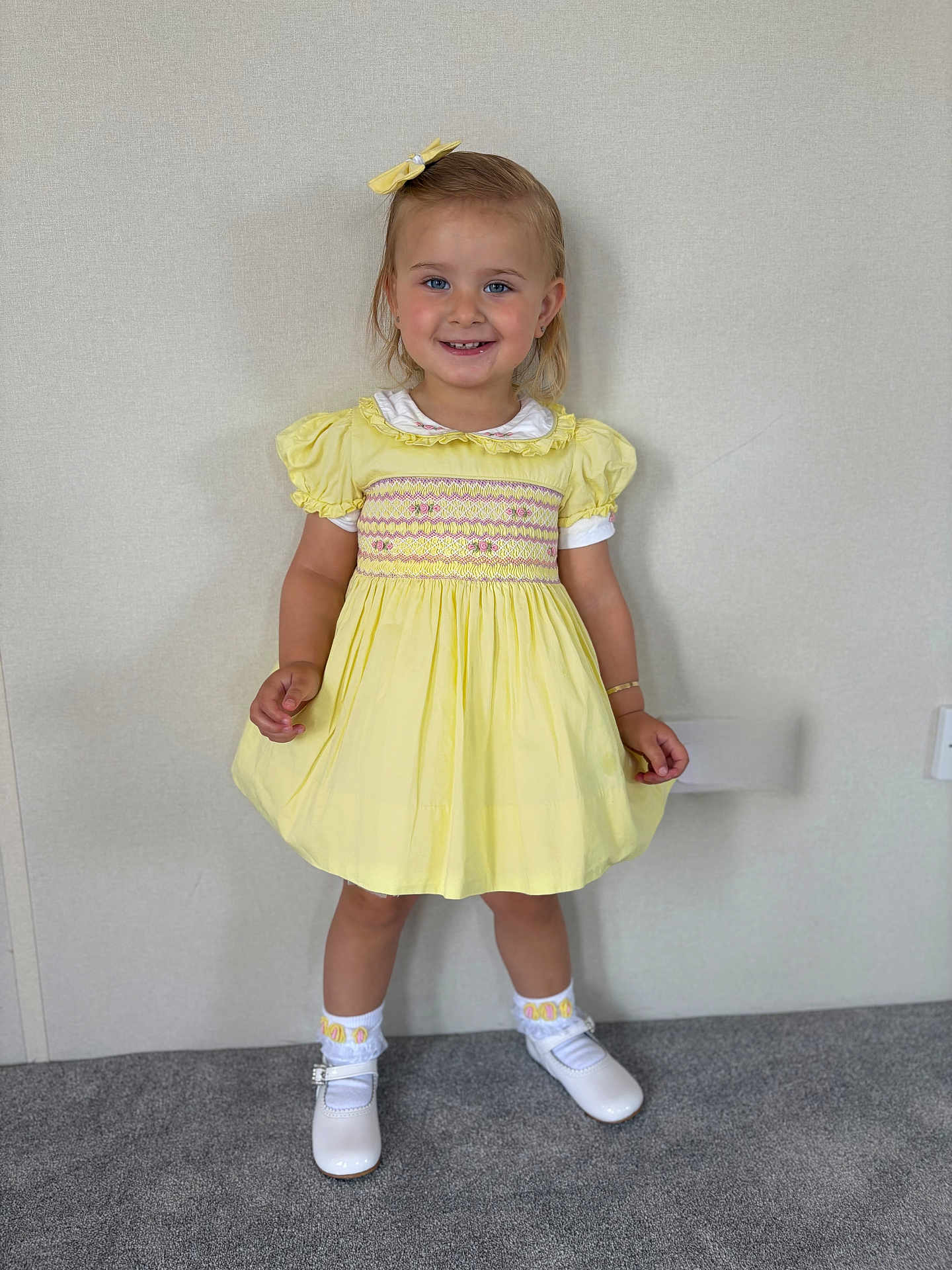 Christiana joined the competition — help win amazing prizes! child, girl, yellow_dress, bow, smile, white_shoes, socks, standing, carpet, indoor, portrait, happy, cute, face, short_hair, light_background, bracelet, fashion, young, person