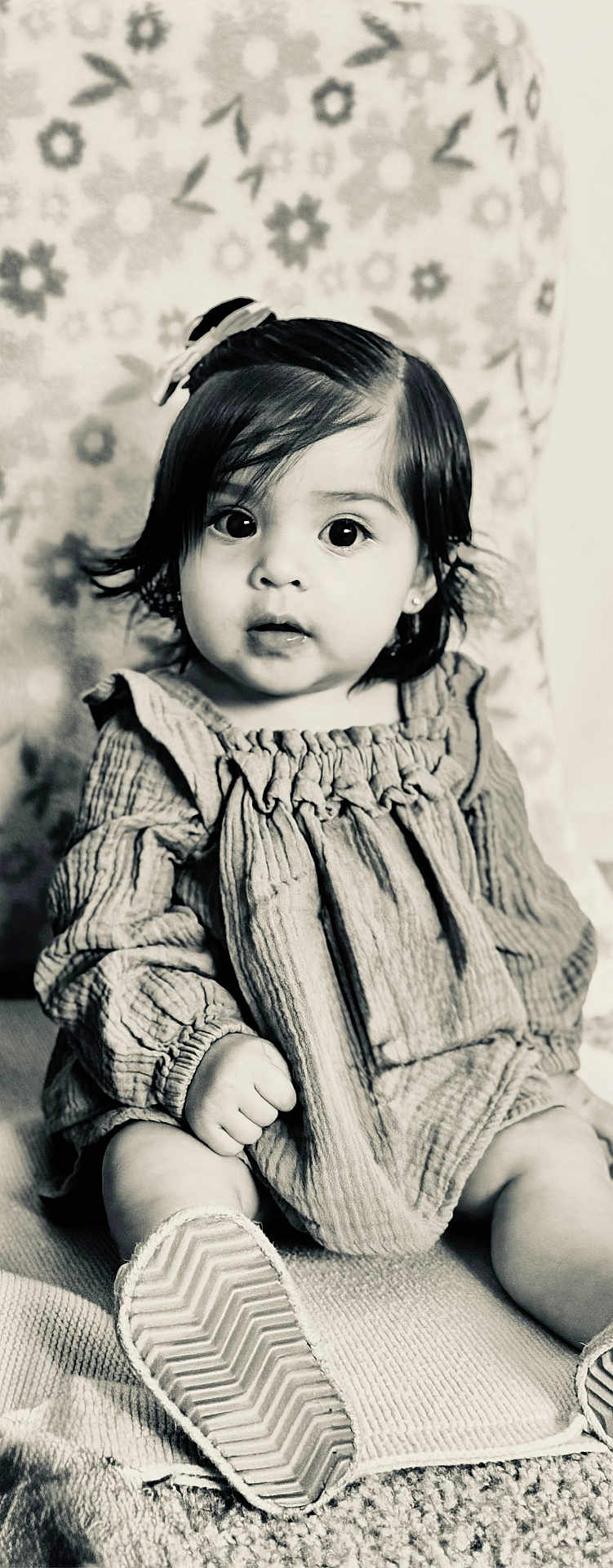 Ariella is registered to the contest to win money with this photo: baby, child, portrait, black_and_white, sitting, dress, shoe, blanket, pattern, indoor, cute, hair_bow, face, expression, infant, young_child, person, texture, closeup, monochrome