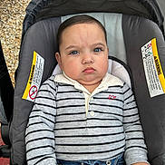 Ismael is registered to the contest to win money with this photo: baby, child, stroller, striped_shirt, jeans, serious_expression, face, person, clothing, hands, seat, warning_label, outdoor, casual, portrait, cute, infant, young_child, sitting, closeup