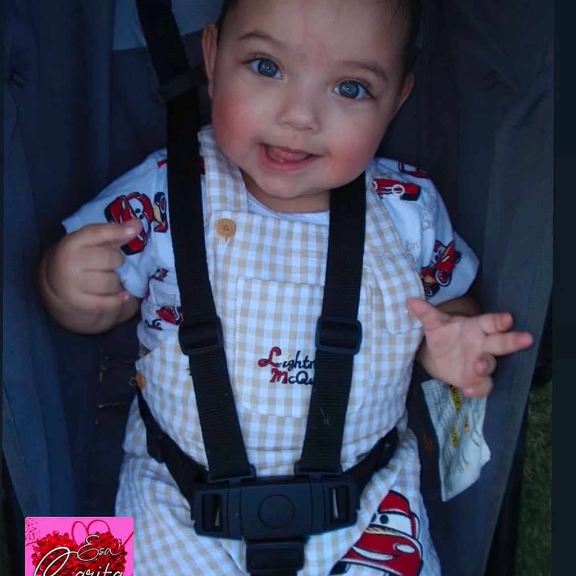 Ismael joined the competition — help win amazing prizes! baby, child, blue_eyes, smiling, stroller, safety_harness, checkered_overalls, cartoon_cars, cute, happy, face, hand, clothing, outdoor, person, infant, seatbelt, portrait, expression, babywearing