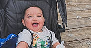 Ismael is registered to the contest to win money with this photo: baby, stroller, blanket, bottle, smiling, happy, child, outdoor, boardwalk, wood, person, clothing, babytrend, blue, cute, infant, face, hand, toddler, daytime