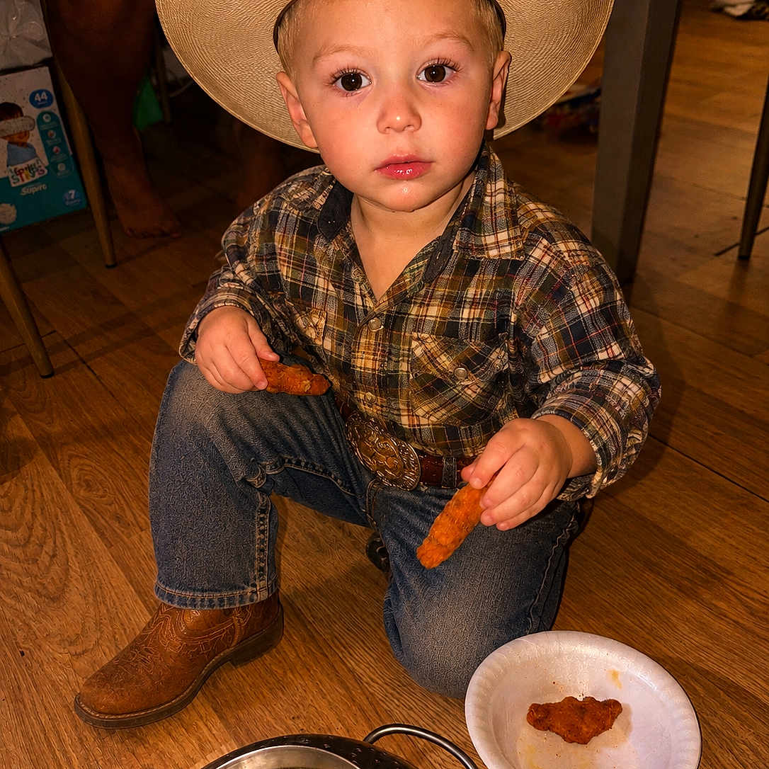 Xzavier joined the competition — help win amazing prizes! child, cowboy_hat, plaid_shirt, jeans, boots, floor, wooden_floor, food, chicken_tenders, paper_plate, colander, indoor, kneeling, person, young_child, snack_time, casual, brown, cute, portrait