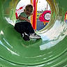 child, toddler, playground, slide, tunnel, smiling, outdoor, play, fun, toy, park, sneakers, jeans, green, plastic, happy, daylight, person, recreation, casual