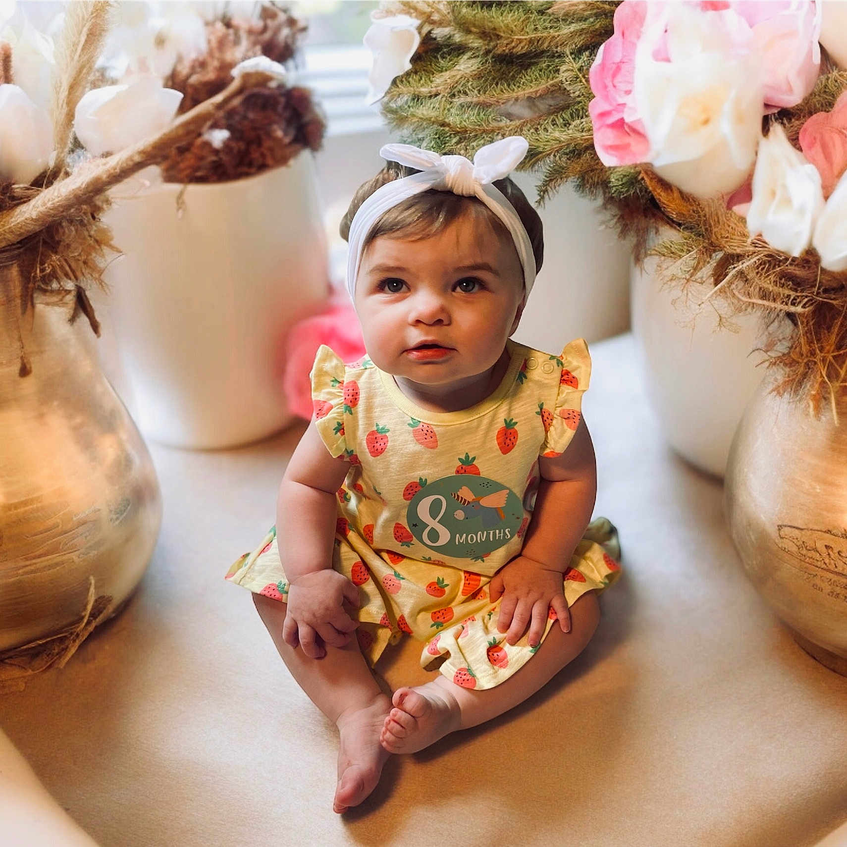 Millacynt is registered to the contest to win money with this photo: adorable, baby, child, curious, cute, decor, dress, dried_flowers, floor, greenery, happy, headband, indoors, infant, portrait, sitting, soft_lighting, strawberry_print, vase, young_child