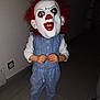 child, mask, clown_mask, costume, indoor, floor, socks, overalls, blue_clothing, white_shirt, hands, toy, scary, halloween, portrait, standing, red_hair, face_covering, dark_background, tile_floor