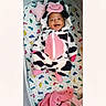baby, infant, child, smiling, cow_costume, cow_hat, onesie, pink, black_and_white, crib, bedding, mattress, nursery, lying_down, portrait, happy, toy, blanket, indoor, colorful