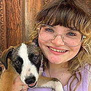 Maxinne joined the competition — help win amazing prizes! woman, puppy, dog, glasses, smile, freckles, curly_hair, holding, closeup, portrait, wooden_door, casual_clothing, happy, outdoor, face, pet, young_adult, light_purple_top, jewelry, friendly