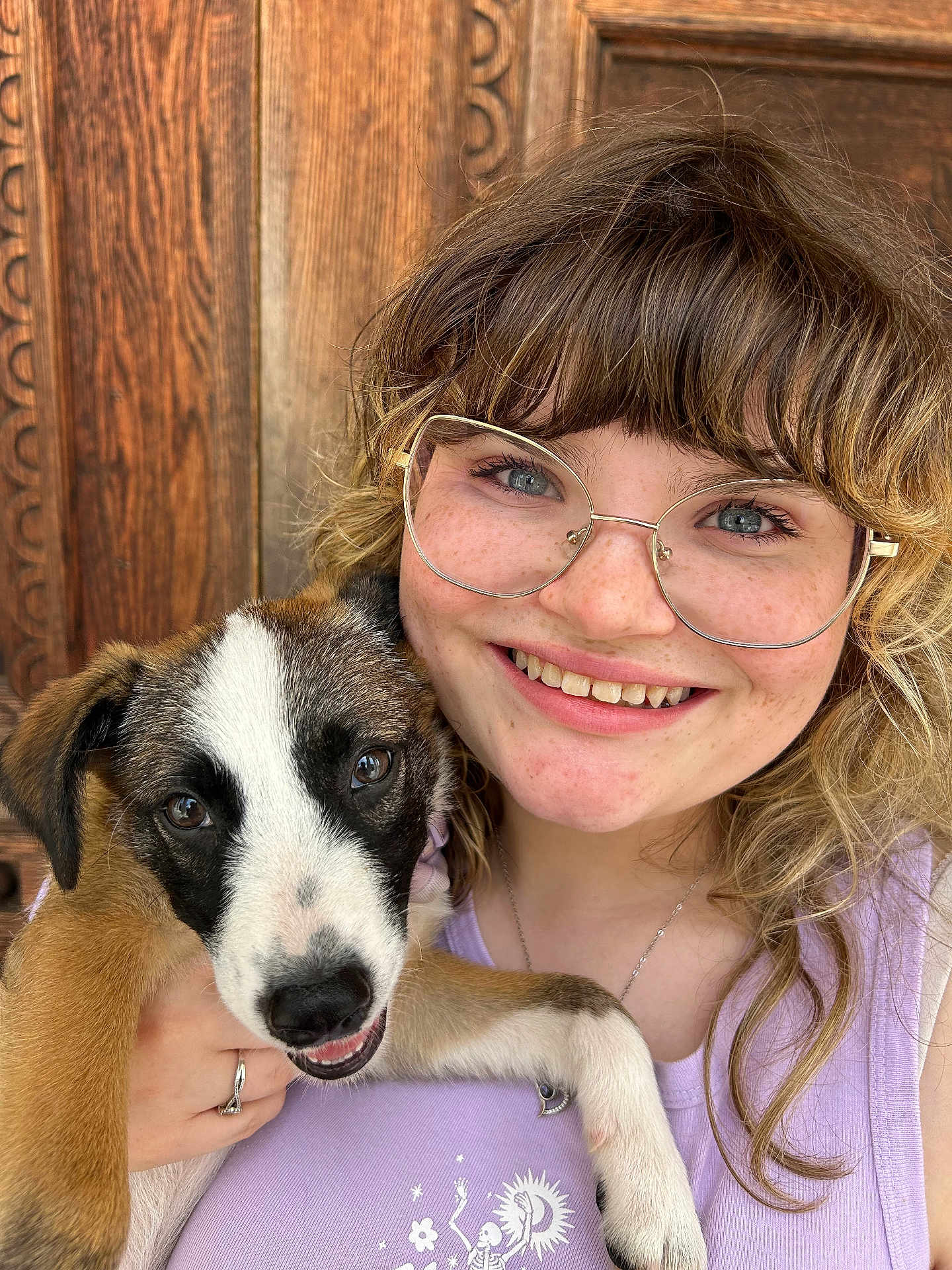 Maxinne joined the competition — help win amazing prizes! woman, puppy, dog, glasses, smile, freckles, curly_hair, holding, closeup, portrait, wooden_door, casual_clothing, happy, outdoor, face, pet, young_adult, light_purple_top, jewelry, friendly