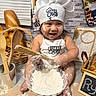 baby, child, chef_hat, flour, baking, kitchen, bowl, wooden_spoon, bread, basket, apron, smiling, sitting, portrait, food, utensils, bakery, indoor, messy, cute