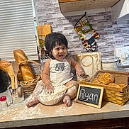 Ryan Mavo joined the competition — help win amazing prizes! child, toddler, baby, baking, flour, kitchen, bread, pastries, bakery, chef, apron, smiling, sitting, countertop, oven_mitt, wooden_utensils, mixing_bowl, chalkboard, indoor, portrait
