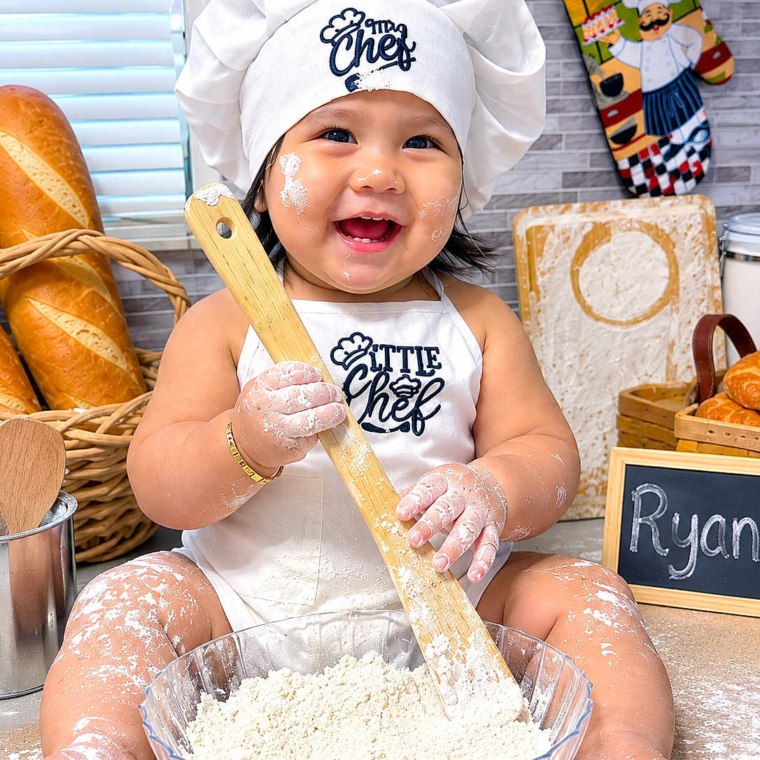 Ryan Mavo is registered to the contest to win money with this photo: baby, child, toddler, chef_hat, apron, smiling, laughing, flour, baking, cooking, wooden_spoon, mixing_bowl, dough, bread, baguette, kitchen, oven_mitt, portrait, sitting, indoor