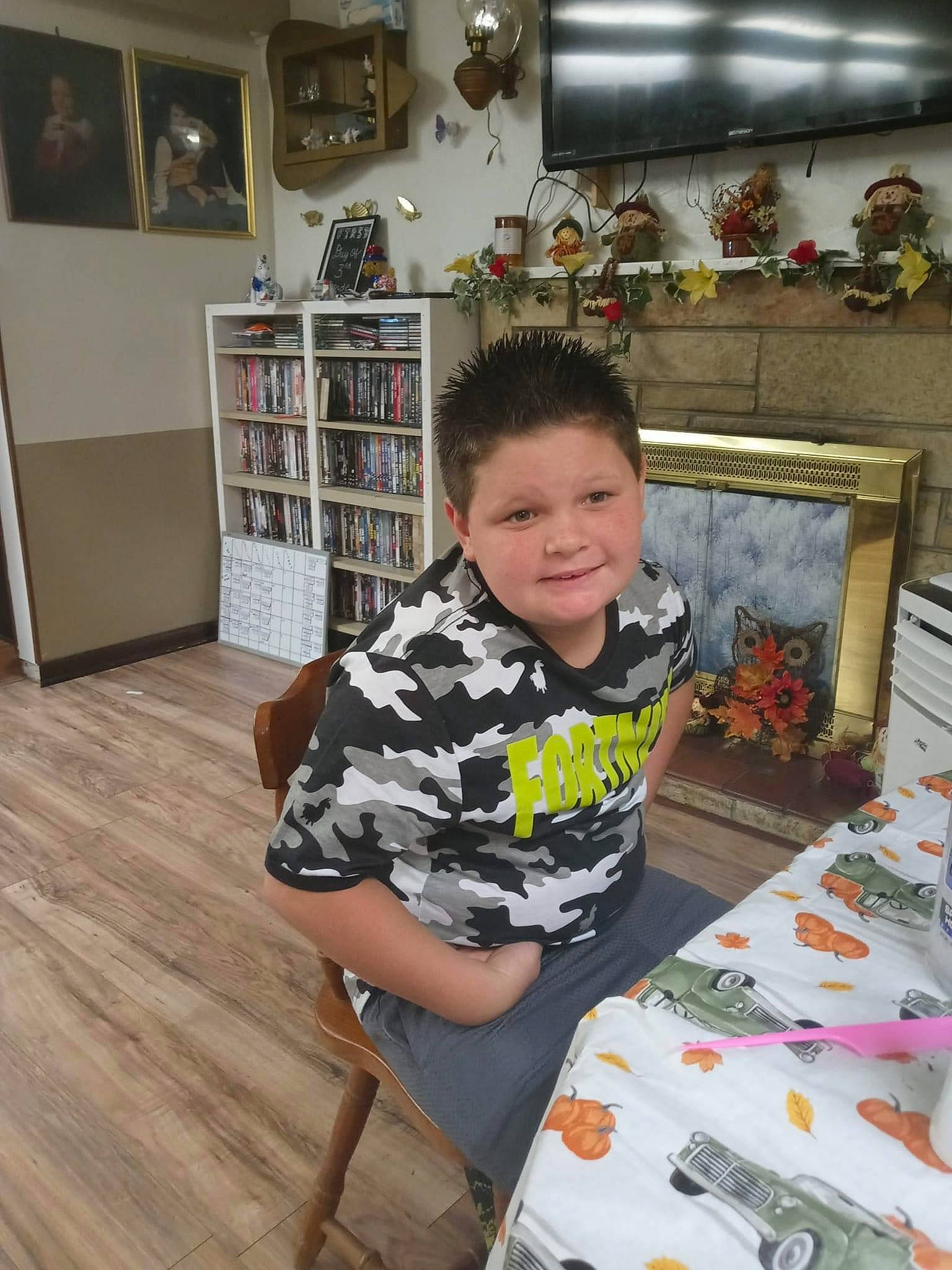 Damian joined the competition — help win amazing prizes! bookcase, chair, child, event, flooring, hardwood, lap, leg, living_room, person, picture_frame, room, shelf, shelving, shorts, sleeve, smile, t_shirt, thigh, toddler