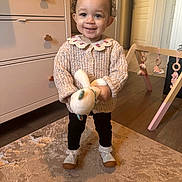 Malia participe au concours pour gagner de l'argent avec cette photo : child, toddler, smiling, indoor, carpet, stuffed_toy, knit_sweater, black_pants, shoes, dresser, wooden_baby_gym, door, floor, toy, curly_hair, home, clothing, person, baby_toy, furniture