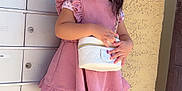 Lucia is registered to the contest to win money with this photo: accessory, bow, child, cute, dress, fashion, girl, hair, happy, mailboxes, outdoor, pink, portrait, purse, sandals, smile, standing, sunlight, wall, wood