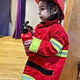 toddler, child, firefighter_costume, red_jacket, helmet, fire_extinguisher, indoor, wooden_floor, purple_curtain, concentration, side_profile, person, toy, reflective_stripes, young_child, costume_play, cute, small_hands, black_hair, standing
