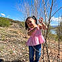 Lucia is registered to the contest to win money with this photo: child, girl, outdoor, nature, sky, blue_sky, rocks, dry_bush, trees, grass, sunlight, smiling, pigtails, pink_top, jeans, shoes, playful, portrait, daytime, landscape