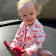 Ellie is registered to the contest to win money with this photo: toddler, child, smiling, toy_guitar, outdoor, trampoline, pink_clothing, butterfly_pattern, sunlight, happy, playful, hair, face, footwear, jacket, person, kids, playing, cute, young_child