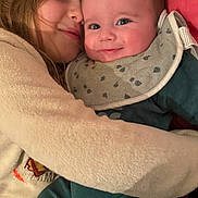 Tyler a rejoint le concours — aidez-le/la à gagner de superbes lots ! baby, child, hug, smile, face, bib, sweater, cozy, warm, affection, happy, closeup, portrait, indoor, red_background, cute, family, love, toddler, comfort