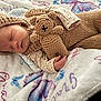 baby, bedtime, blanket, butterfly_pattern, child, cozy, crocheted_toy, cute, handmade, indoors, infant, knitted_clothing, peaceful, portrait, resting, sleeping, small_hands, soft_texture, teddy_bear, warm