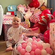 Ivy-Mai joined the competition — help win amazing prizes! baby, child, balloons, presents, toys, pink, white, floor, gift_wrap, smiling, indoor, celebration, net, wooden_floor, ball, cute, happy, decorations, sitting, playful