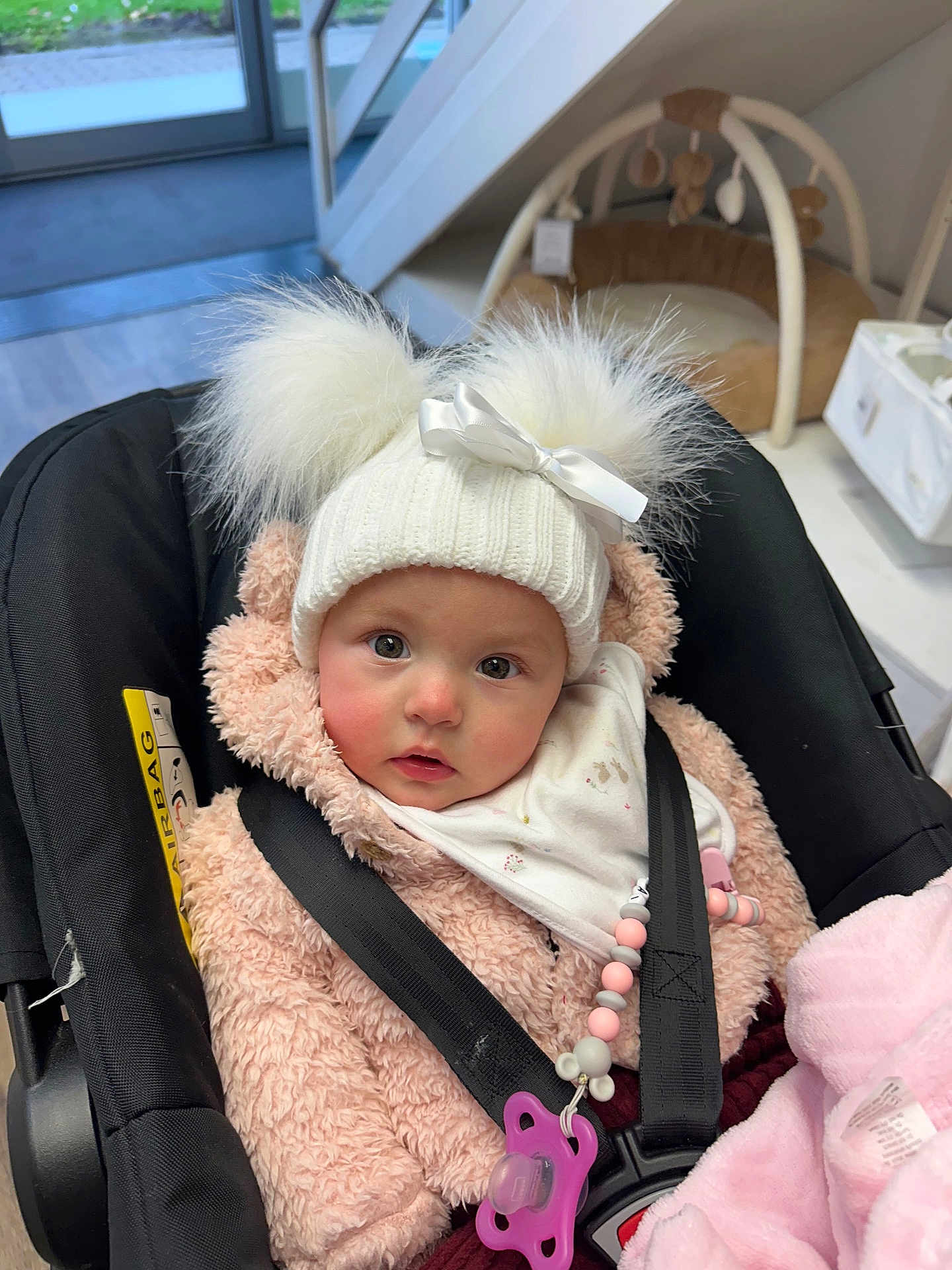 Ivy-Mai joined the competition — help win amazing prizes! baby, child, car_seat, hat, pom_poms, bow, pink_jacket, blanket, pacifier, beads, indoors, face, eyes, winter_clothing, cute, infant, soft_toys, warm_clothing, seatbelt, curious_expression