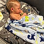 baby, sleeping, blanket, playpen, mesh, dinosaur_print, animal_print, cushion, infant, child, soft_texture, bedtime, cozy, peaceful, indoor, pale_skin, blond_hair, pacifier, nap, rest