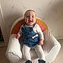 baby, child, smiling, denim_dress, white_tights, black_shoes, armchair, rainbow_pattern, indoor, happy, cute, sitting, person, face, head, furniture, floor, wall, home, cozy