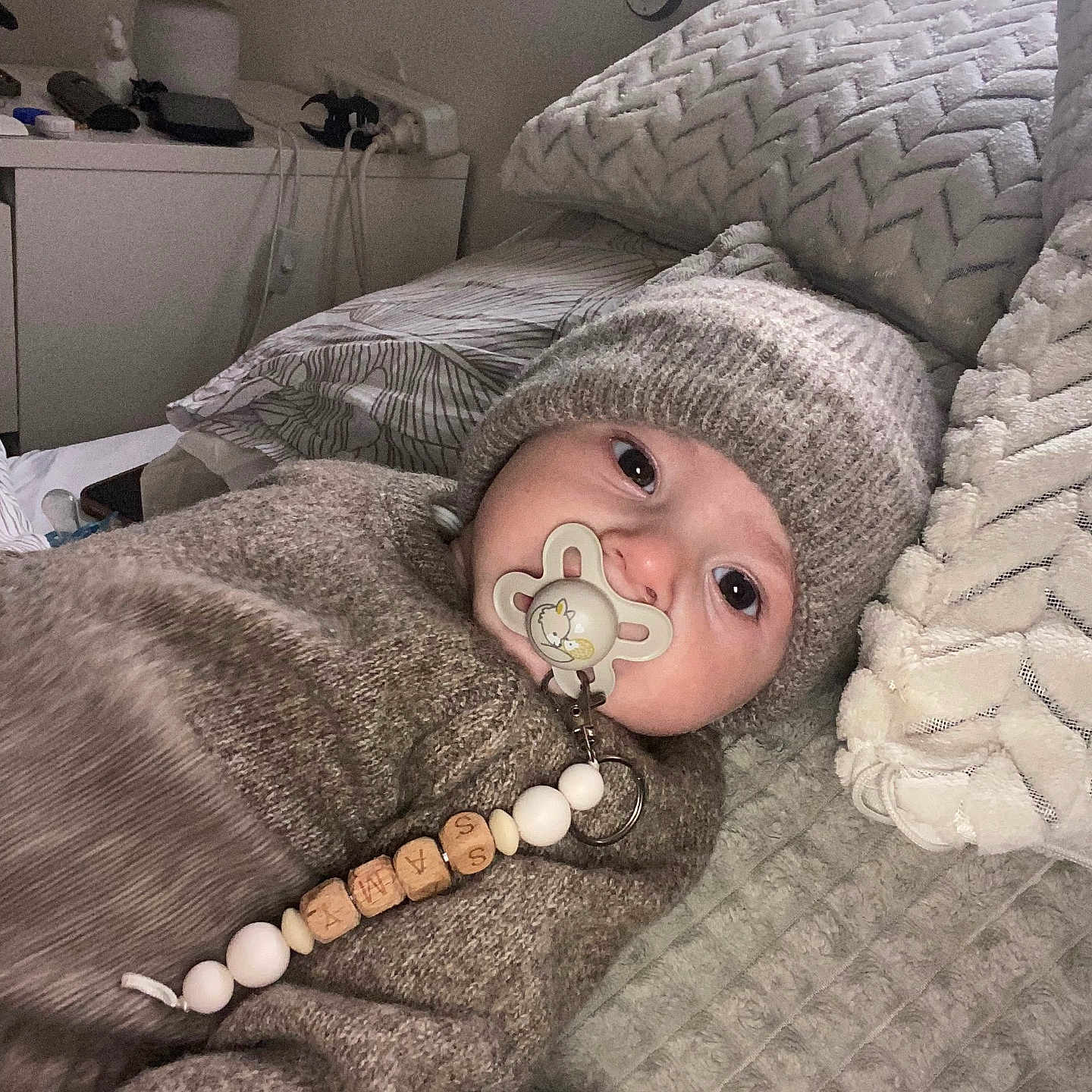 Samy a rejoint le concours — aidez-le/la à gagner de superbes lots ! baby, bedroom, blanket, child, closeup, comfort, cute, face, indoor, infant, knitted_hat, knitted_sweater, lying_down, pacifier, person, pillow, resting, soft_texture, warm_clothing, young_child