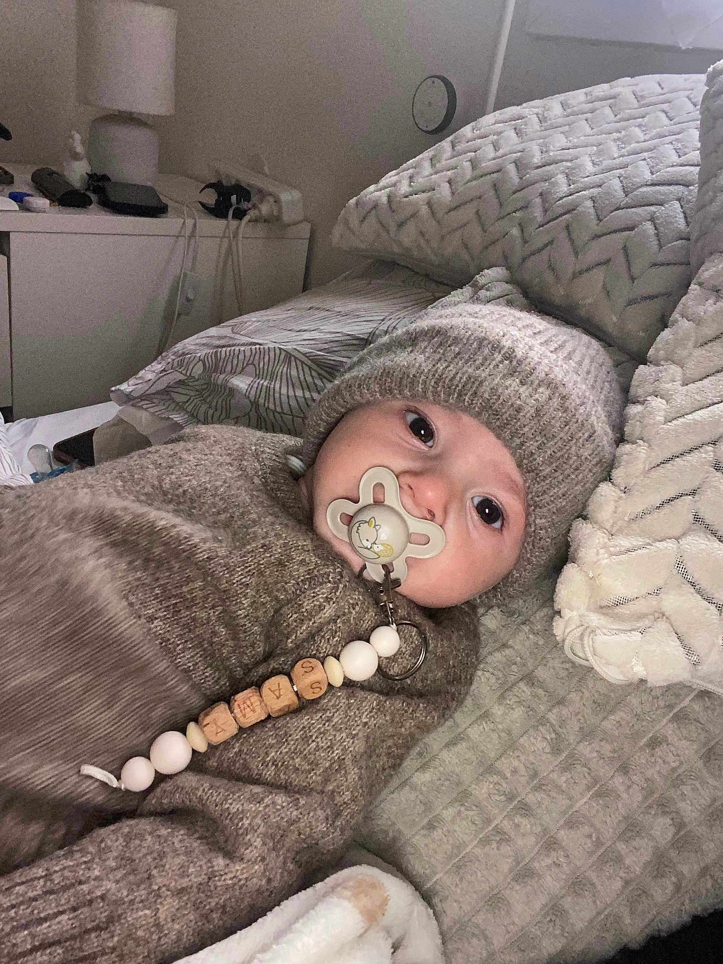 Samy a rejoint le concours — aidez-le/la à gagner de superbes lots ! baby, infant, pacifier, knitted_hat, knitted_sweater, blanket, pillow, bedroom, indoor, child, cute, lying_down, face, closeup, warm_clothing, comfort, soft_texture, person, resting, young_child