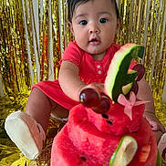 Gybell Gómez joined the competition — help win amazing prizes! baby, child, watermelon, cake, fruit, grapes, cucumber, strawberry, headband, dress, pink, celebration, party, gold_backdrop, curious, sitting, closeup, food, table, footwear