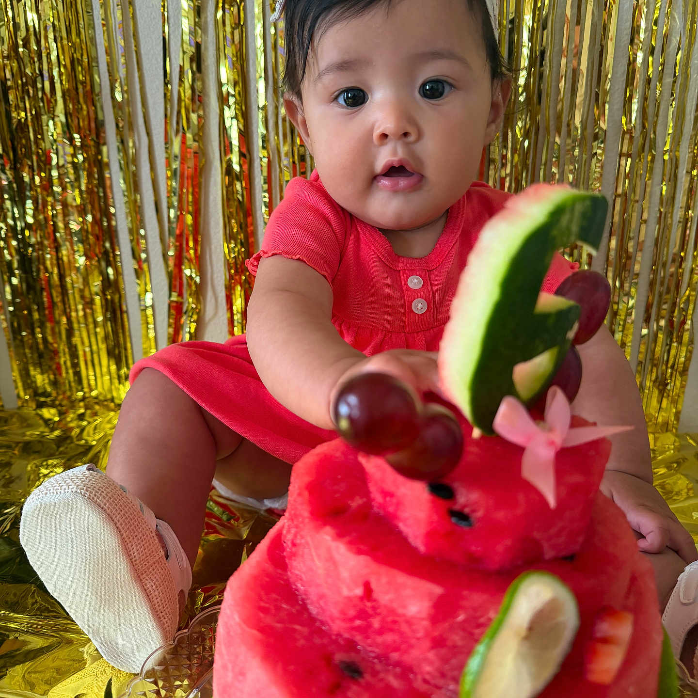 Gybell Gómez joined the competition — help win amazing prizes! baby, child, watermelon, cake, fruit, grapes, cucumber, strawberry, headband, dress, pink, celebration, party, gold_backdrop, curious, sitting, closeup, food, table, footwear