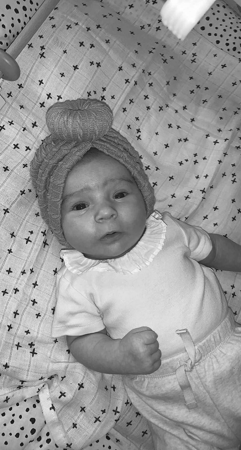 Thaïs a rejoint le concours — aidez-le/la à gagner de superbes lots ! baby, baby_toddler_clothing, black, black_and_white, cheek, child, comfort, eye, facial_expression, gesture, happy, head, headwear, outerwear, person, photograph, skin, sleeve, standing, textile