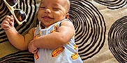 Jakai is registered to the contest to win money with this photo: baby, smiling, infant, clothing, sunglasses, blanket, pattern, happy, cute, lying_down, toddler, indoor, person, child, apparel, accessory, face, skin, playful, relaxed