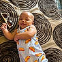 baby, smiling, infant, clothing, sunglasses, blanket, pattern, happy, cute, lying_down, toddler, indoor, person, child, apparel, accessory, face, skin, playful, relaxed