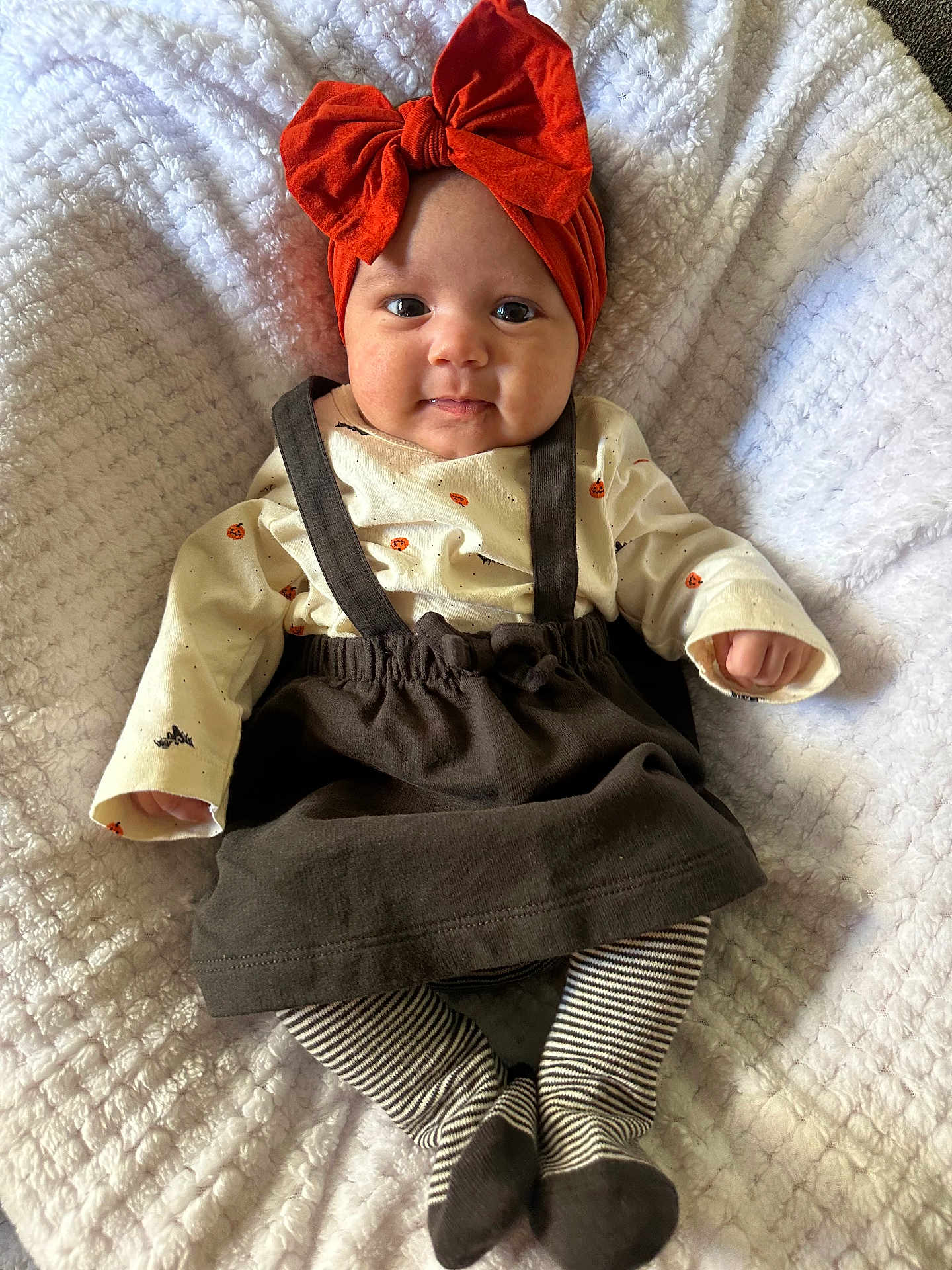 Neilani joined the competition — help win amazing prizes! baby, blanket, child, cozy, cute, headwear, indoors, infant, lying_down, orange_bow, person, portrait, pumpkin_prints, skirt, smiling, soft_texture, striped_socks, suspenders, sweater, white_blanket