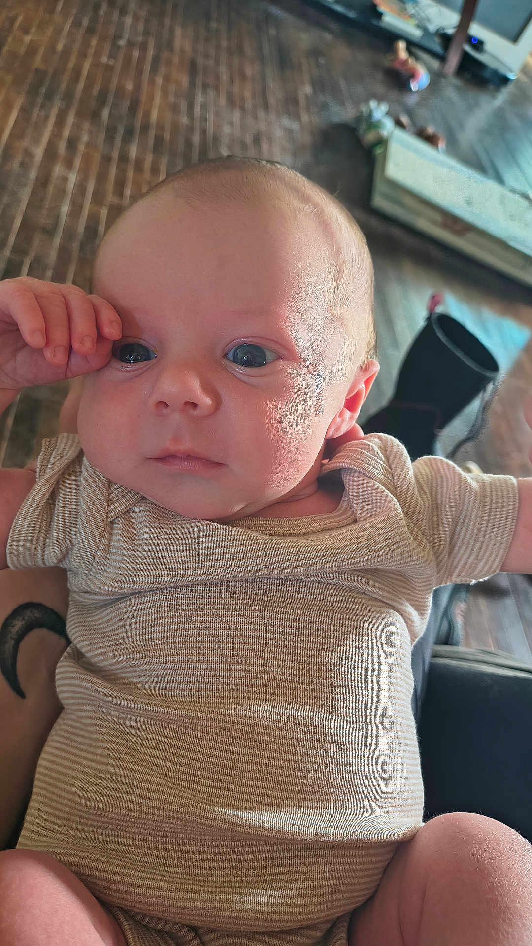 Noah is registered to the contest to win money with this photo: baby, infant, face, eyes, hand, onesie, striped_clothing, skin, person, portrait, cute, indoor, floor, wooden_floor, blurred_background, curious, expression, newborn, child, young